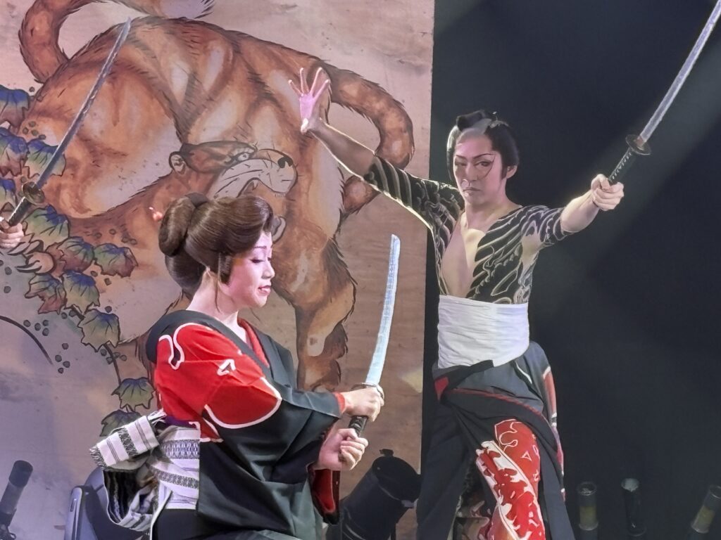 Two Taishuu Theatre performers acting in a samurai sword fight scene, dressed in traditional Japanese costumes.