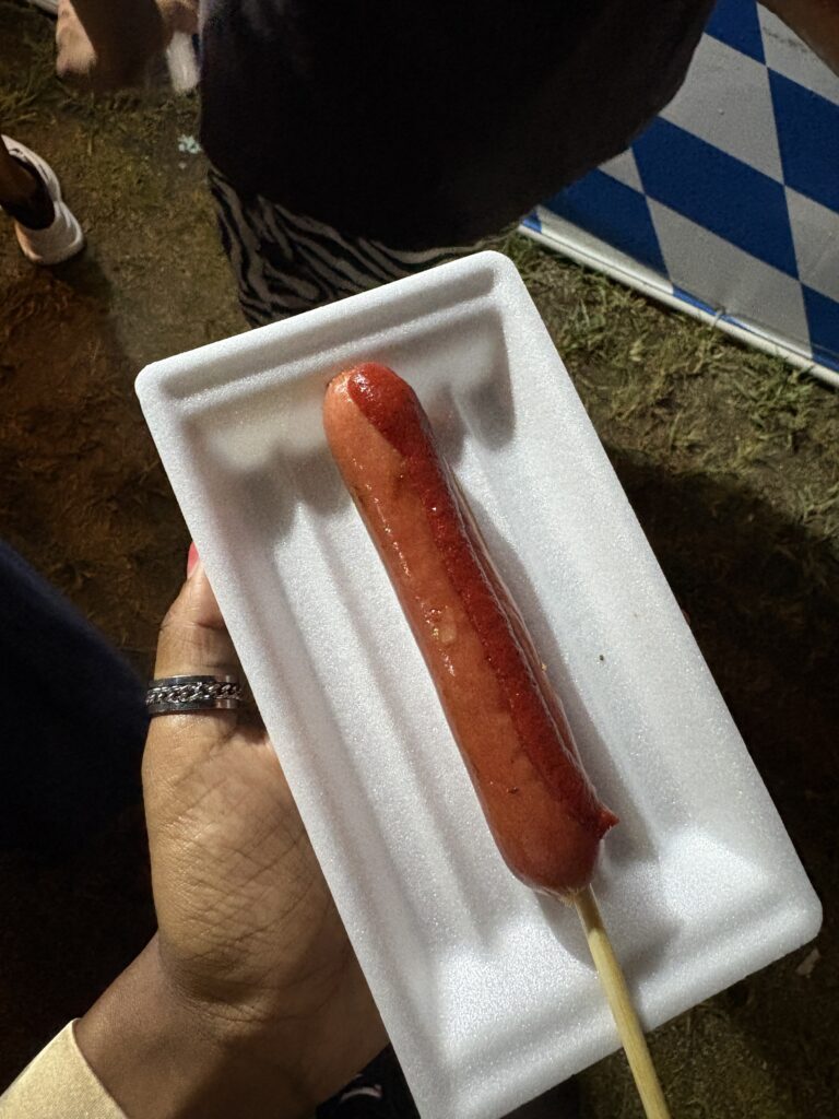 Close-up of a sausage on a stick served on a white tray.
