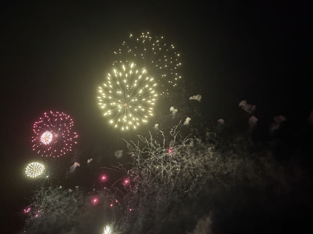 Bright yellow and pink fireworks exploding above the ocean.