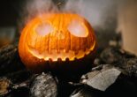 Carved jack-o’-lantern glowing with smoke coming from its mouth and eyes, placed on logs.