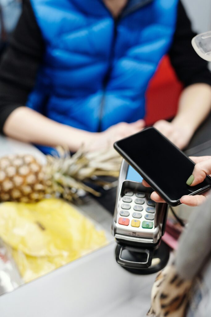A customer using a smartphone to make a contactless payment at a grocery store counter.