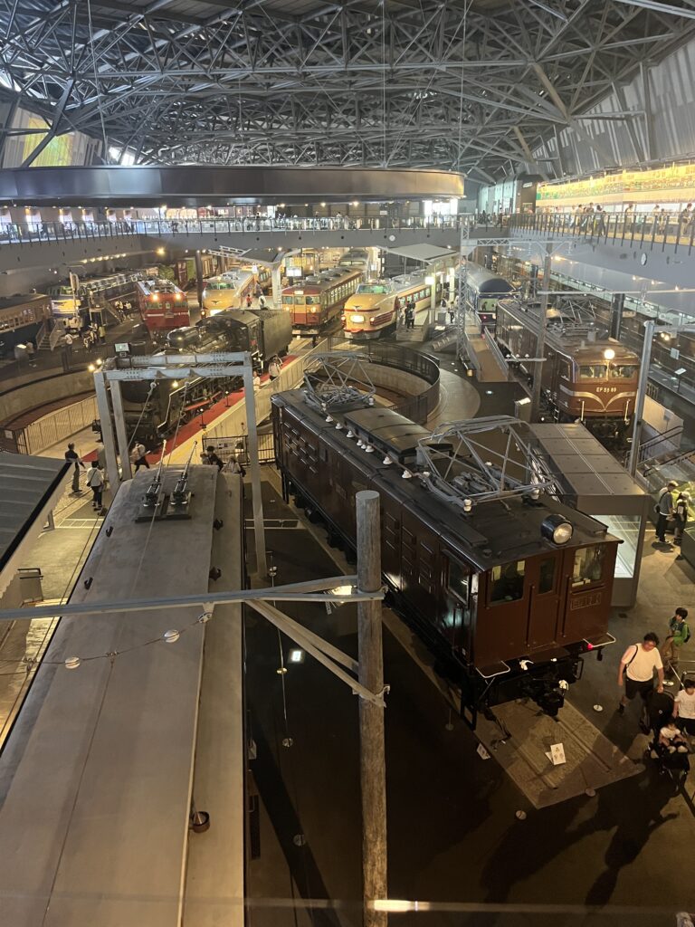 A panoramic view of the museum’s main hall showcasing dozens of historical trains, from steam locomotives to modern express models, under a vast steel roof.
