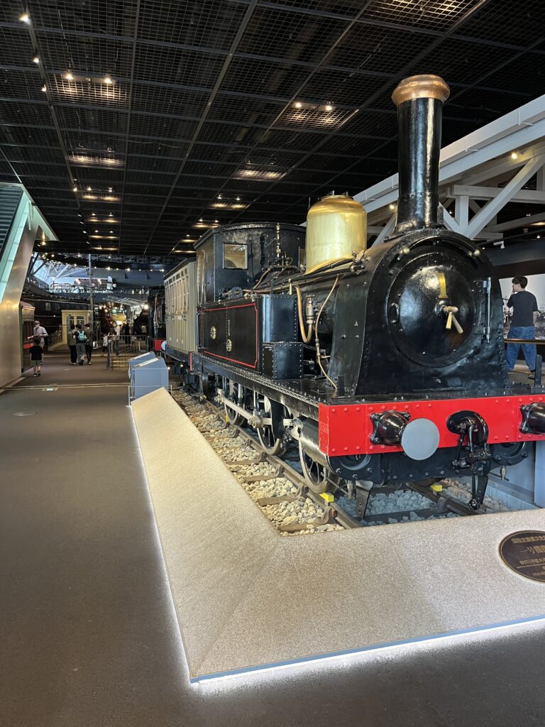 A restored black steam locomotive with brass details and a red front plate, displayed indoors on a short section of track.