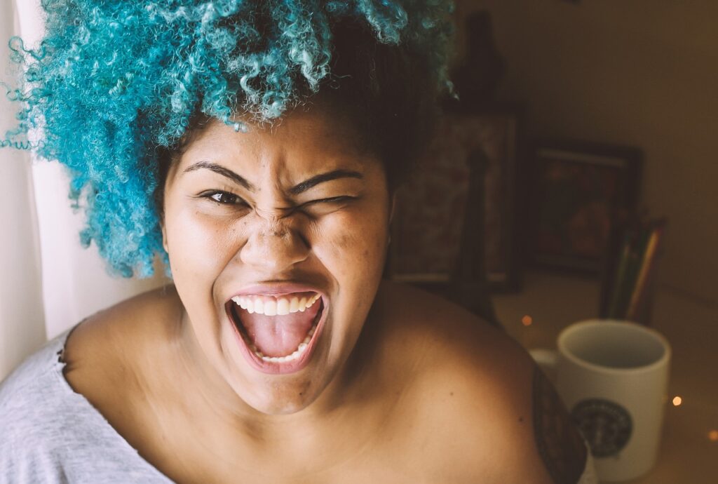 Woman with vibrant blue curly hair smiling and winking at the camera