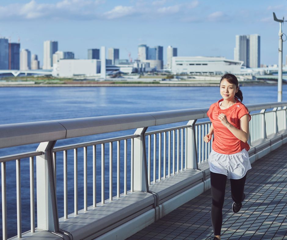 Woman jogging along a riverside pathway in Tokyo with the city skyline in the background.