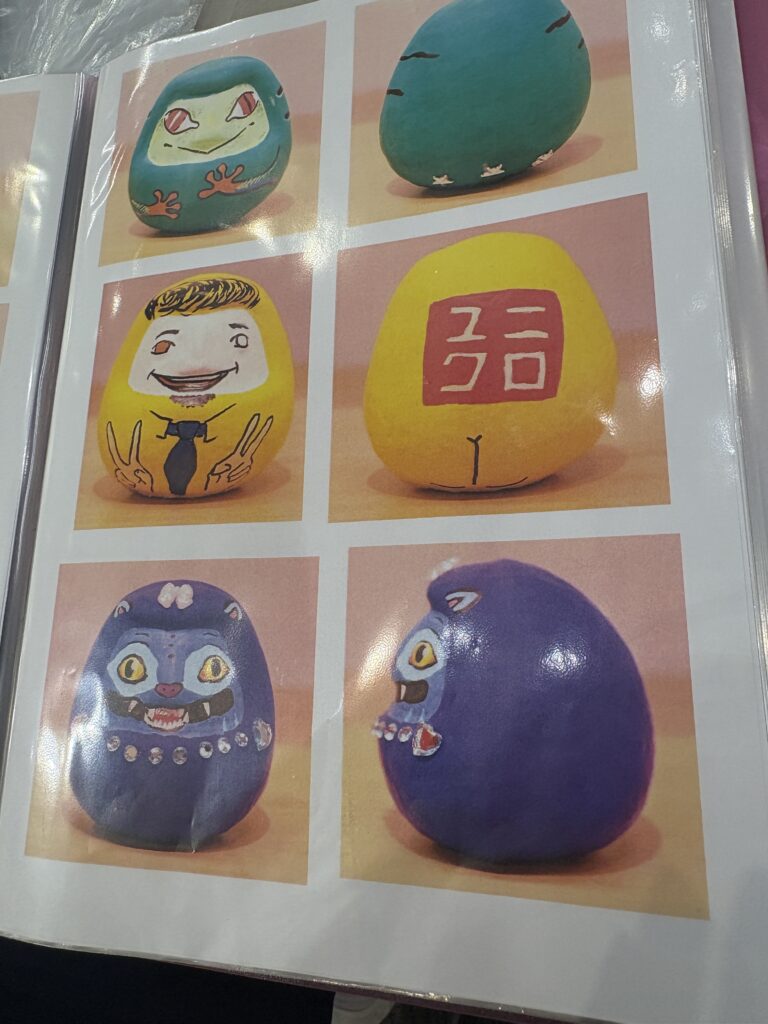 A photo album page showing several uniquely painted daruma dolls, including character-inspired and animal-themed designs.