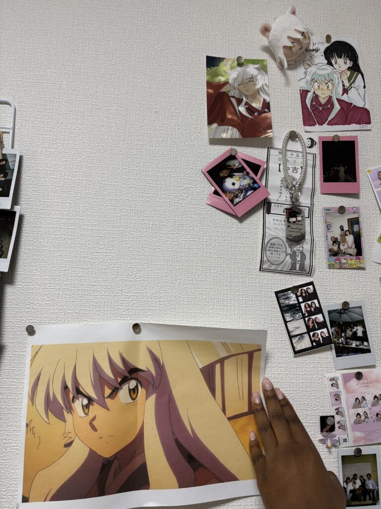 A wall decorated with Inuyasha-themed prints, character drawings, small photos, and memorabilia, with a hand holding a larger print of an Inuyasha character at the bottom.