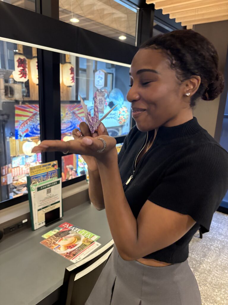 Woman holding a paper crane indoors, smiling softly.