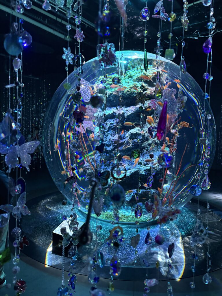 A glowing spherical aquarium decorated with hanging crystals and colorful fish swimming inside.