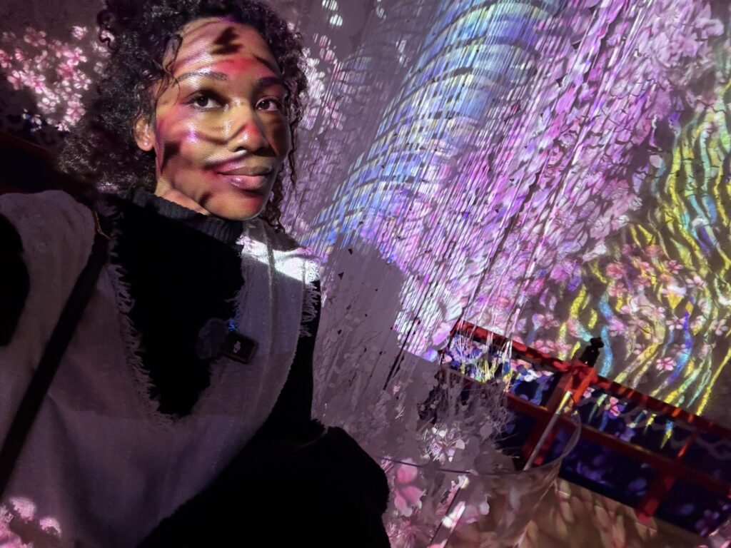 A person standing on a glass floor above colorful fish swimming under purple lighting at ATOA Aquarium.