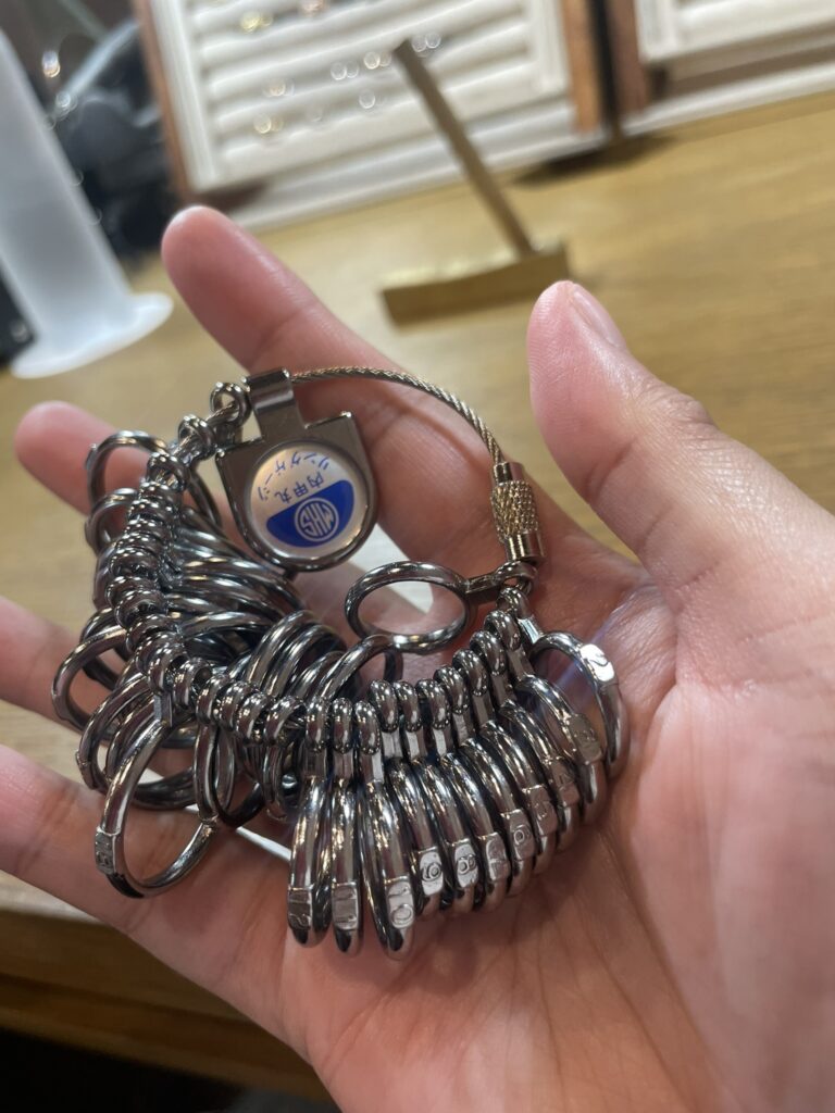 A close-up of a hand holding a ring-sizer tool with multiple metal ring samples attached