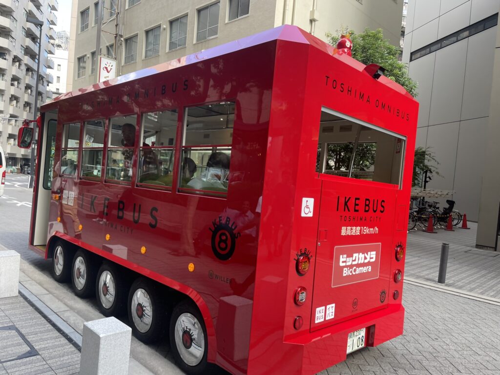 Bright red Ikebus parked on the street in Ikebukuro with passengers inside.