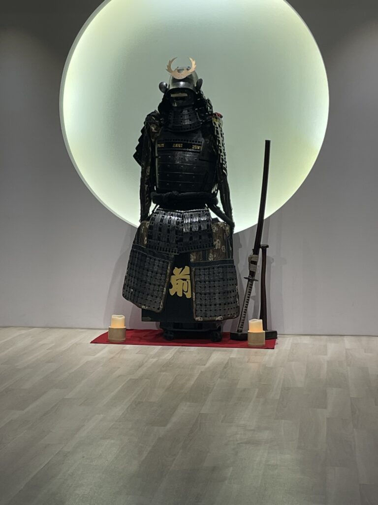 Samurai armor displayed against a round illuminated background in a dojo.