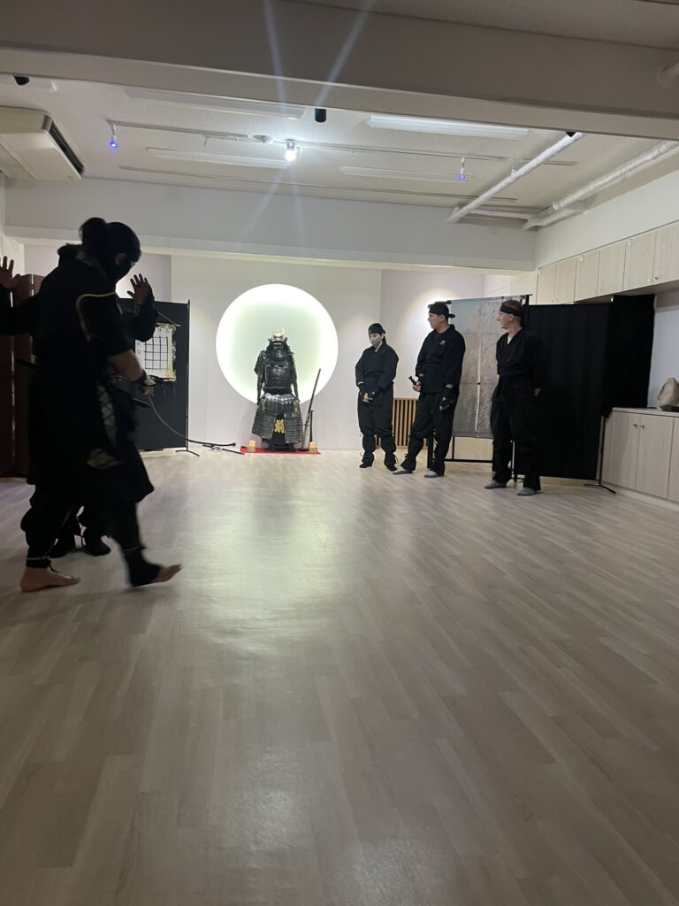 A group of people in ninja outfits inside a dojo with a samurai armor display.