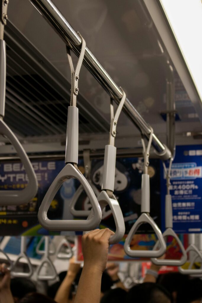 Rows of train hand straps hanging from the ceiling, with passengers’ hands gripping them during a crowded ride.