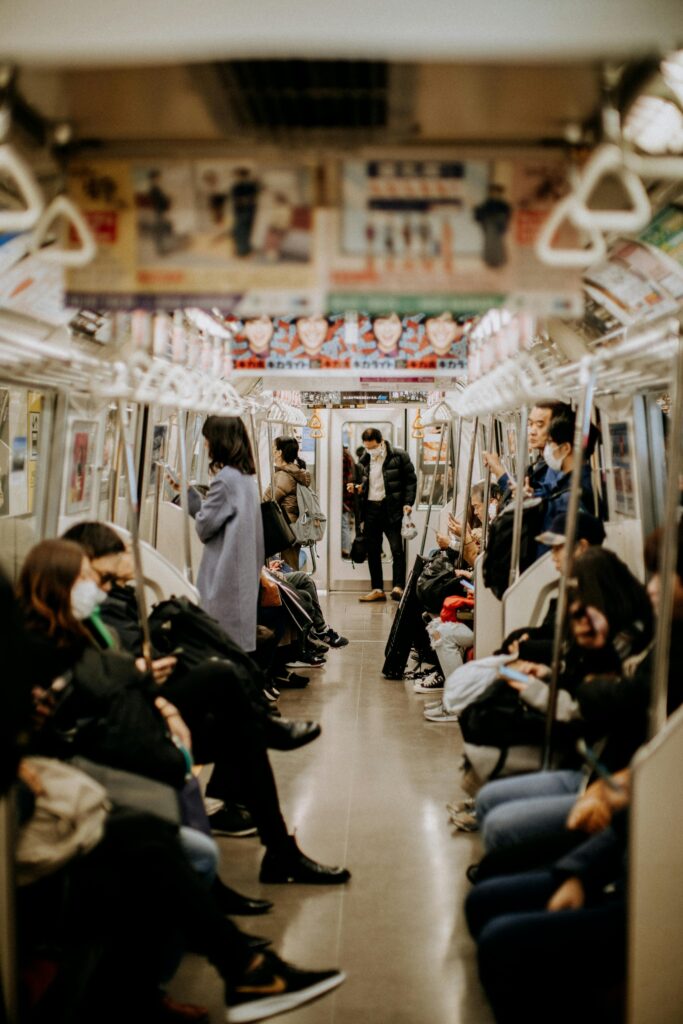 A view inside a Japanese train with seated passengers, some standing, as the train moves through the city.