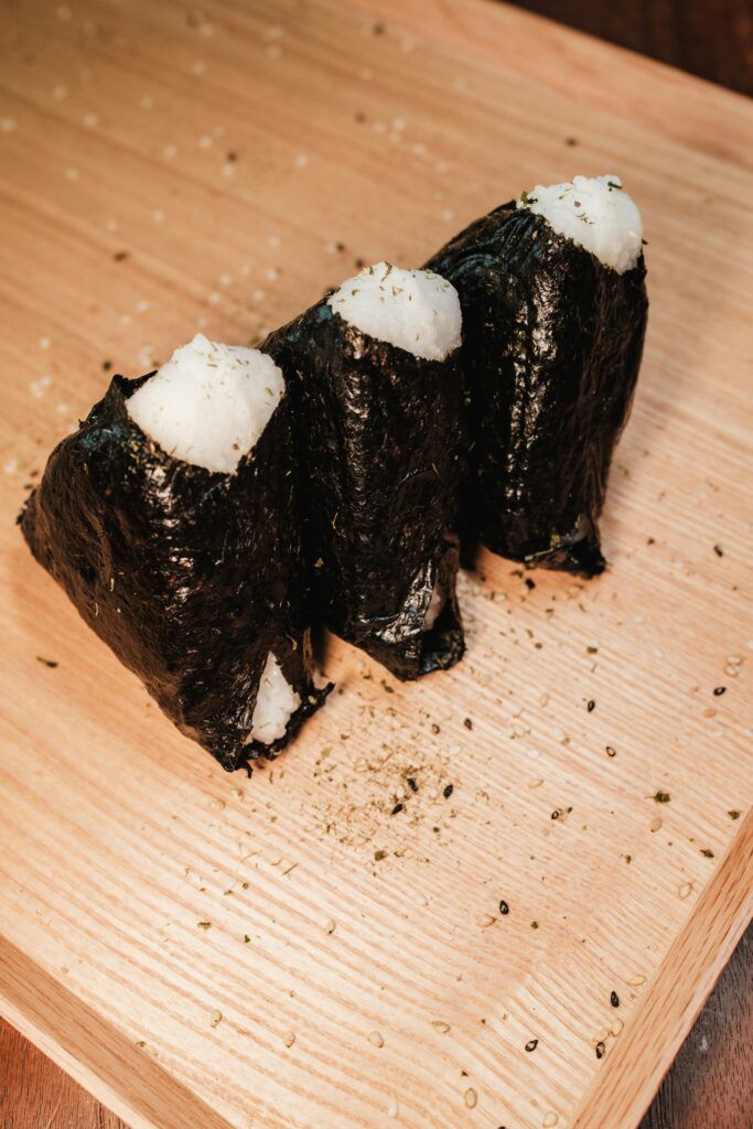 Three triangular onigiri wrapped in nori, neatly arranged on a wooden board sprinkled with sesame seeds.