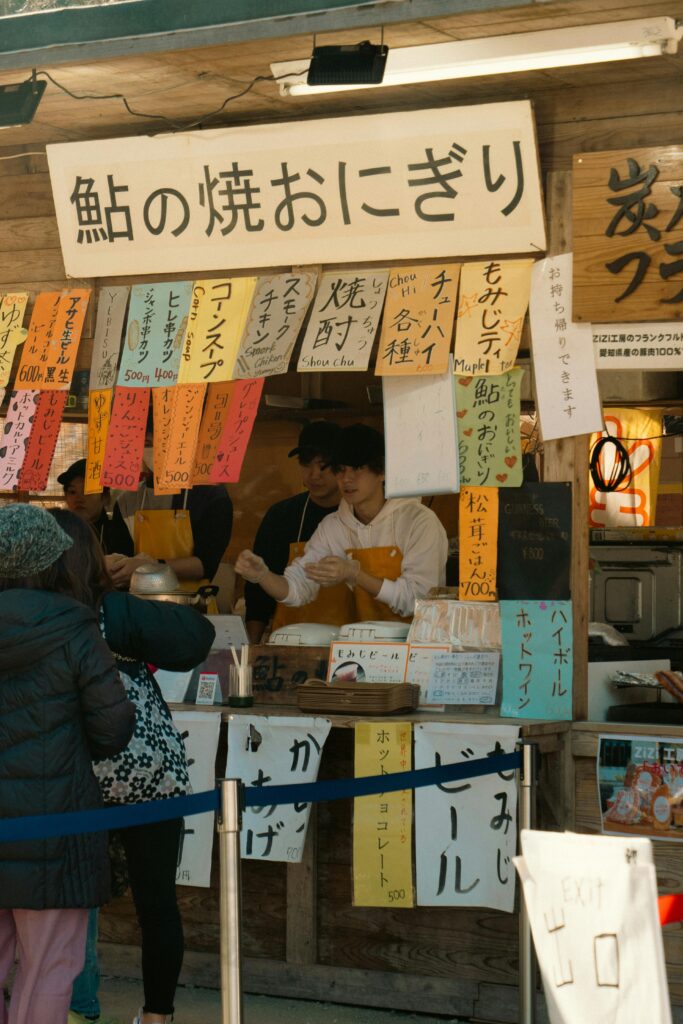 A small Japanese food stall selling freshly made onigiri with colorful handwritten signs.