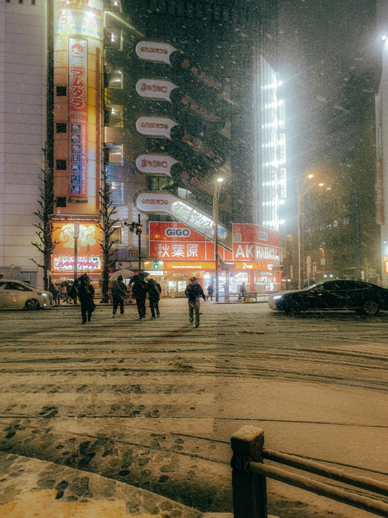 People walking through heavy snow at a busy Tokyo intersection at night.