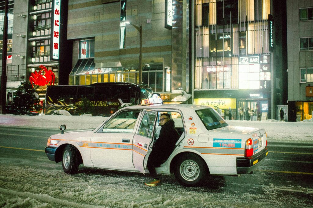 A taxi driver sitting in an idling cab surrounded by heavy snow on a Tokyo street.