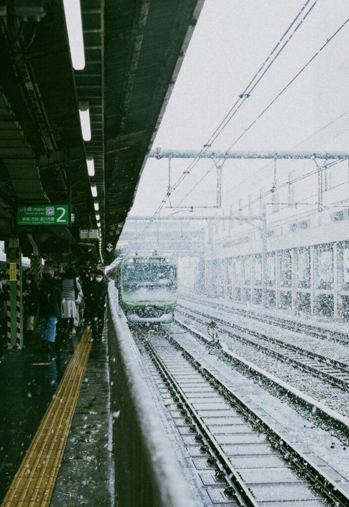 Yamanote Line train approaching a snowy platform filled with commuters.