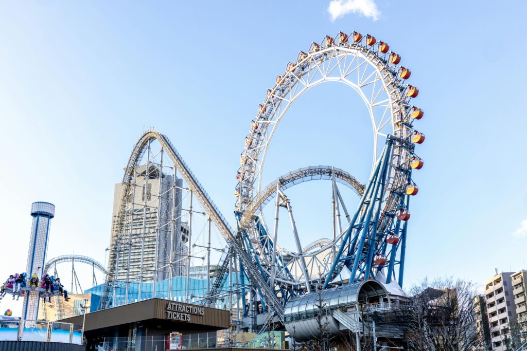The colorful Ferris wheel and roller coaster at Tokyo Dome City amusement park under a bright blue sky.