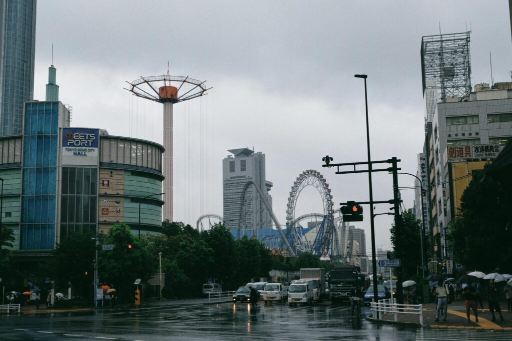 Rainy street view of Tokyo Dome City with visible roller coaster tracks and the Meets Port building.