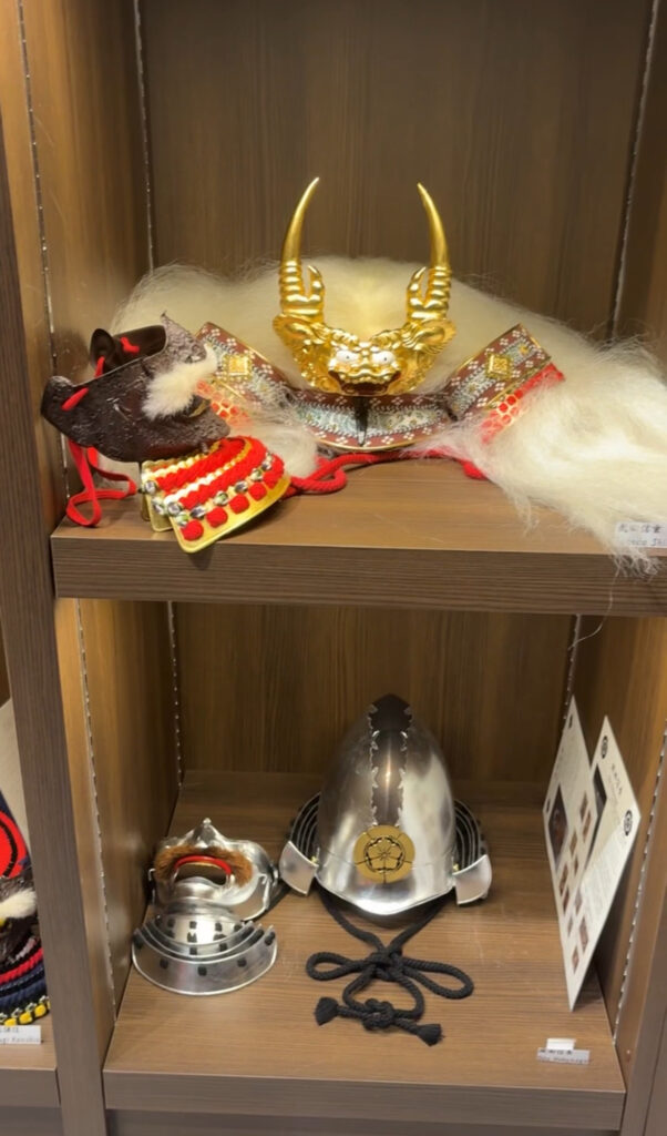 A shelf displaying ornate samurai helmets and masks at Michi Cultural Center in Osaka.