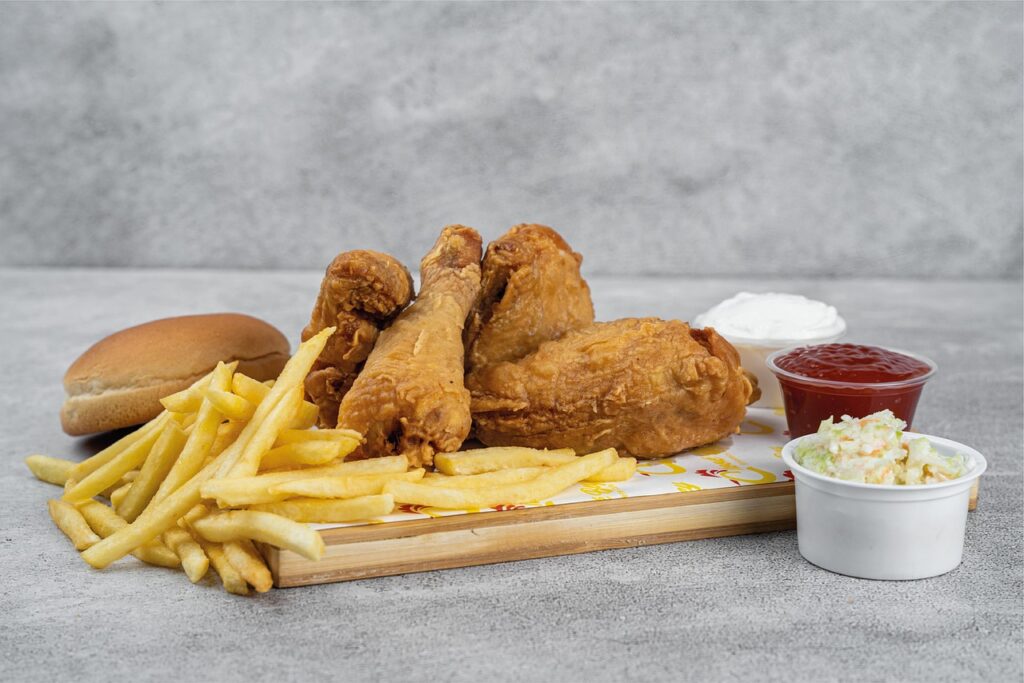 A plate of fried chicken served with French fries, a bun, coleslaw, ketchup, and a small cup of sauce on a light gray background Christmas
