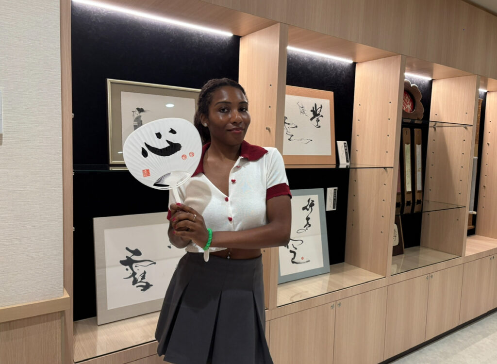 A woman holding a hand-painted uchiwa fan with Japanese calligraphy inside Michi’s gallery area.