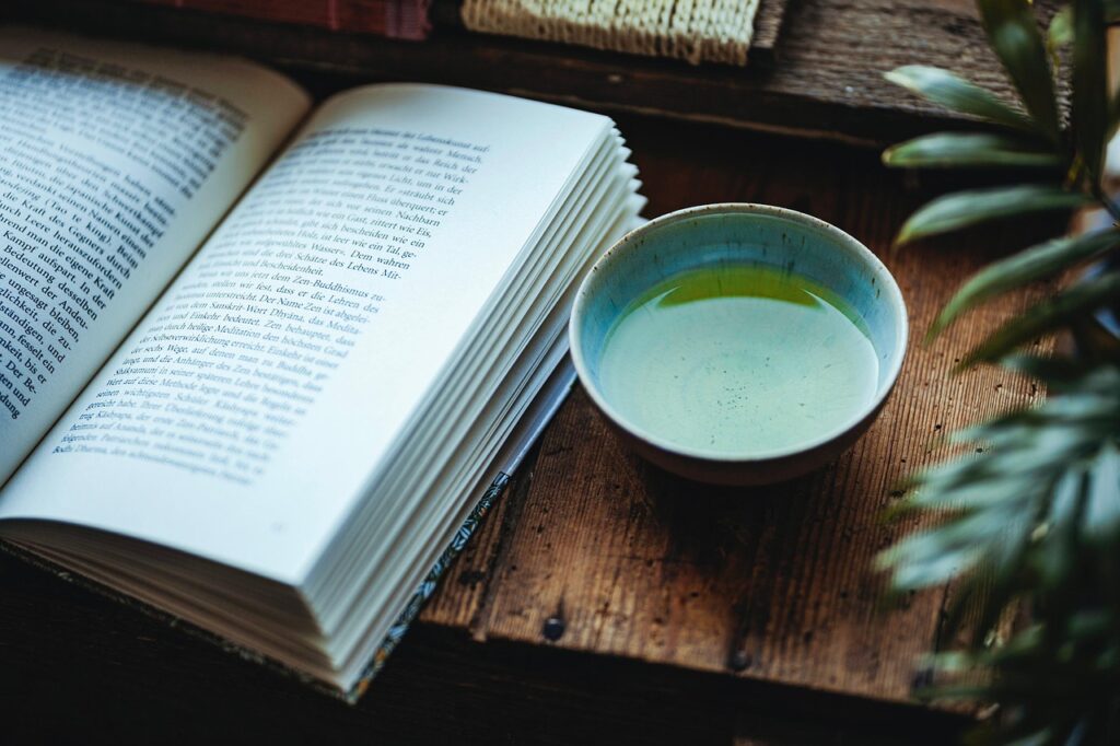 Open book and a cup of green tea on a wooden table, creating a calm and mindful reading atmosphere.
