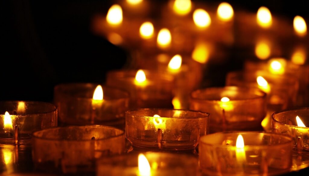 Rows of small glowing candles creating a warm and intimate golden light in a dark setting.
