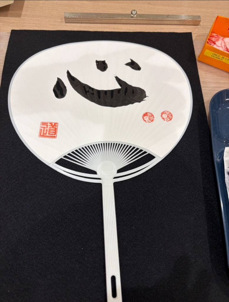 A close-up of a white uchiwa fan featuring hand-painted Japanese calligraphy.