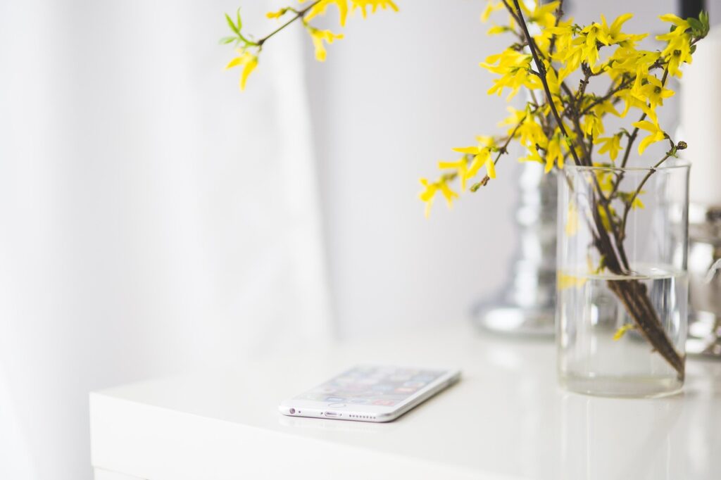 Minimalist white table with a smartphone and yellow flowers in a glass vase, symbolizing digital detox and mindful living.