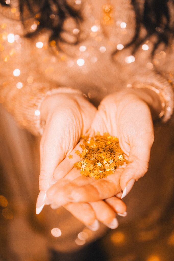 A pair of hands gently cupping golden star-shaped glitter with warm, festive bokeh lights in the background Christmas