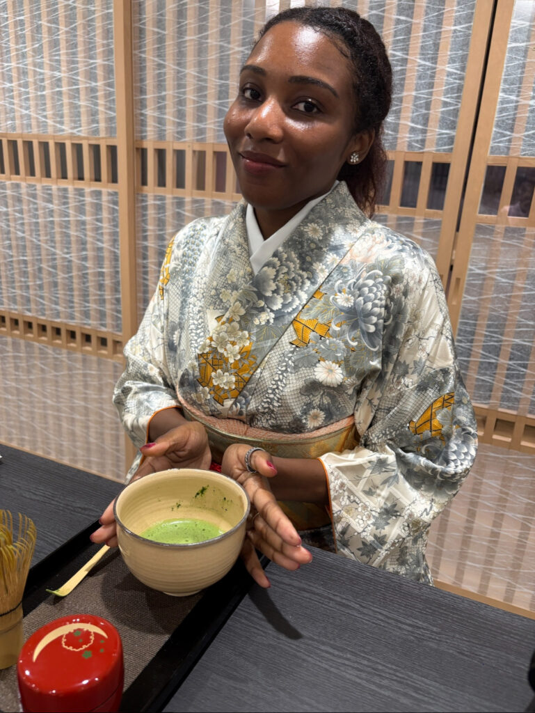 A woman dressed in a silver and gold kimono holding a bowl of matcha during the tea ceremony at Michi.