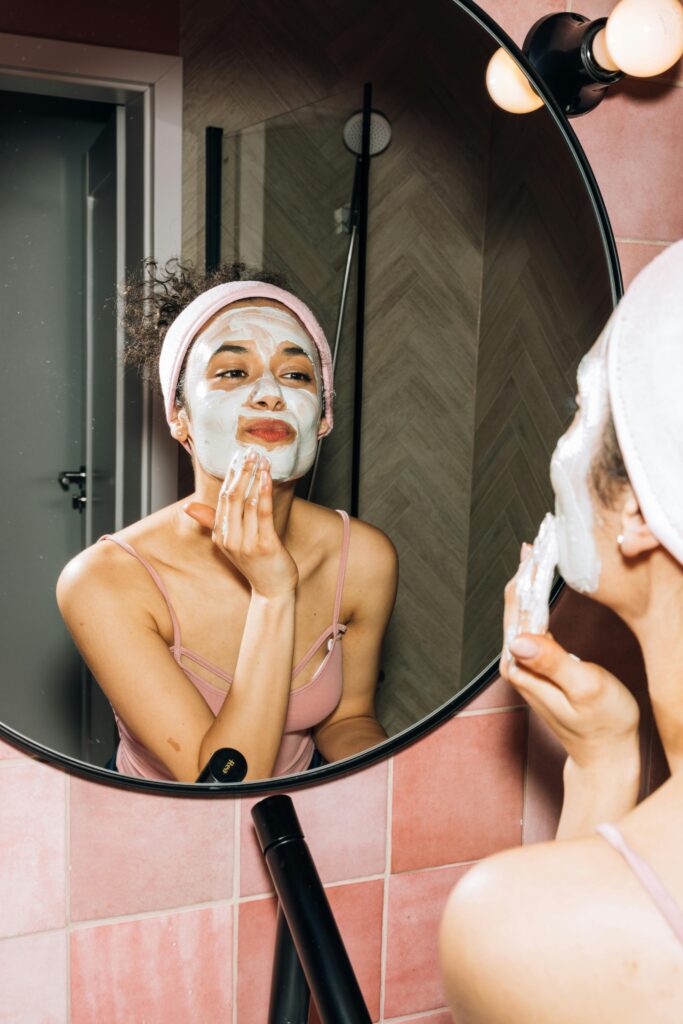 Woman applying a white face mask while looking in a mirror