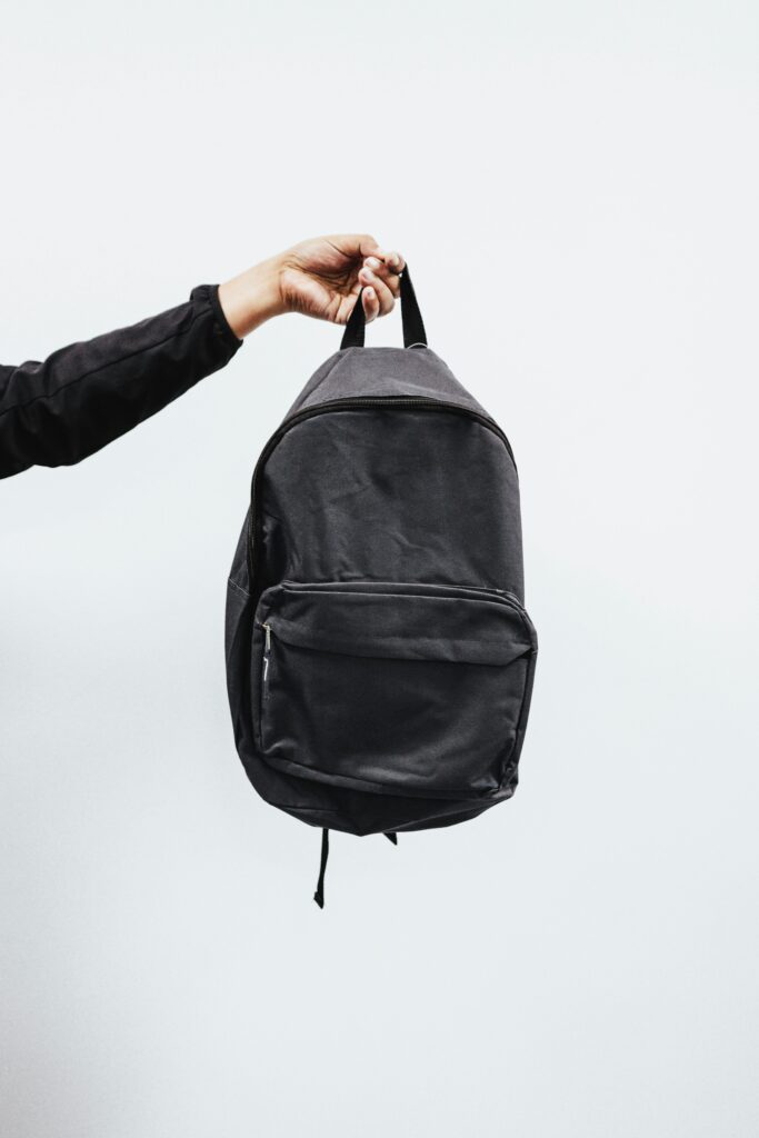 Hand holding a black emergency backpack against a plain white background.
