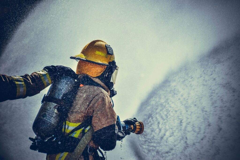 Firefighter in full gear spraying water during an emergency response drill.