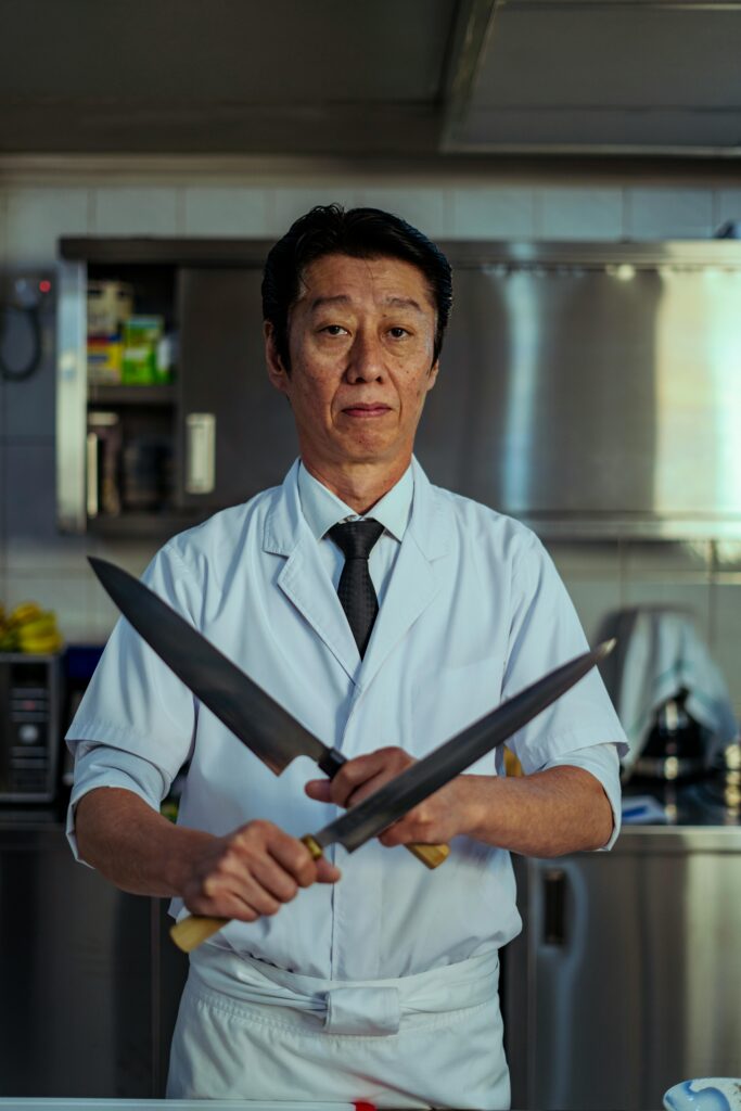 Japanese chef holding two traditional knives in a professional kitchen