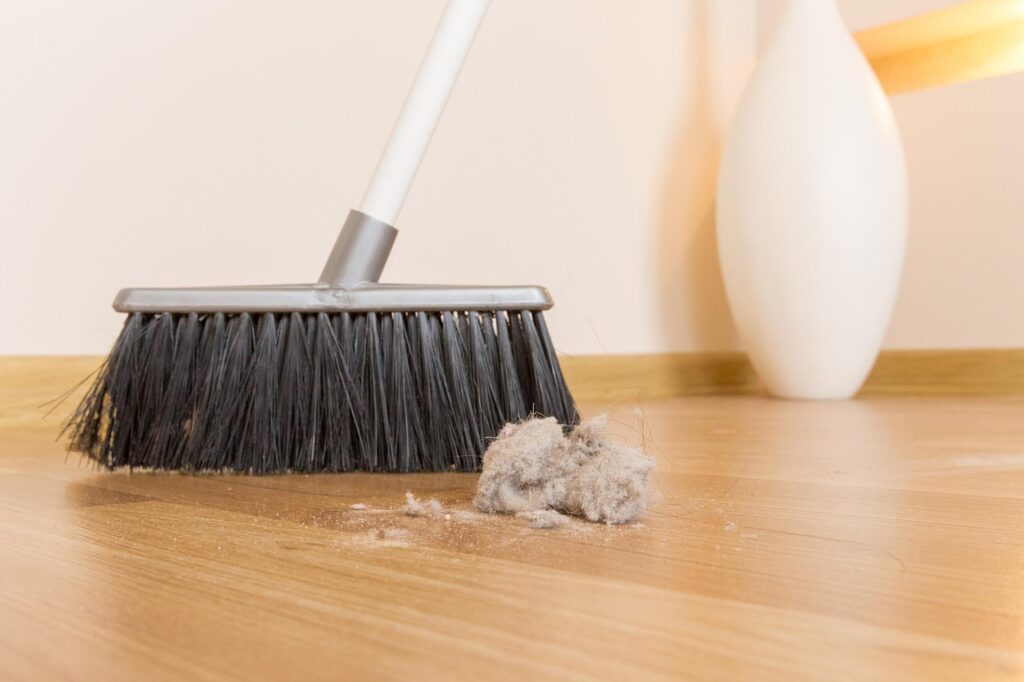 Broom sweeping dust on a wooden floor symbolizing Osoji, the Japanese end-of-year cleaning tradition.