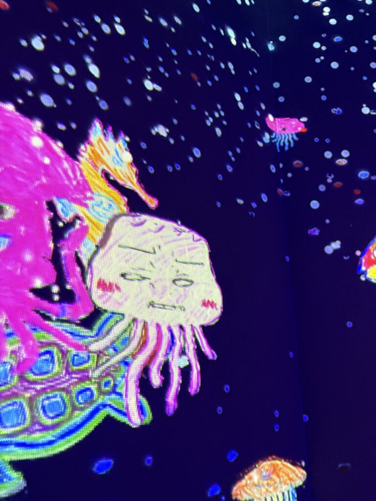 Colorful digital sea creatures including jellyfish and abstract animals swimming across a glowing interactive screen.