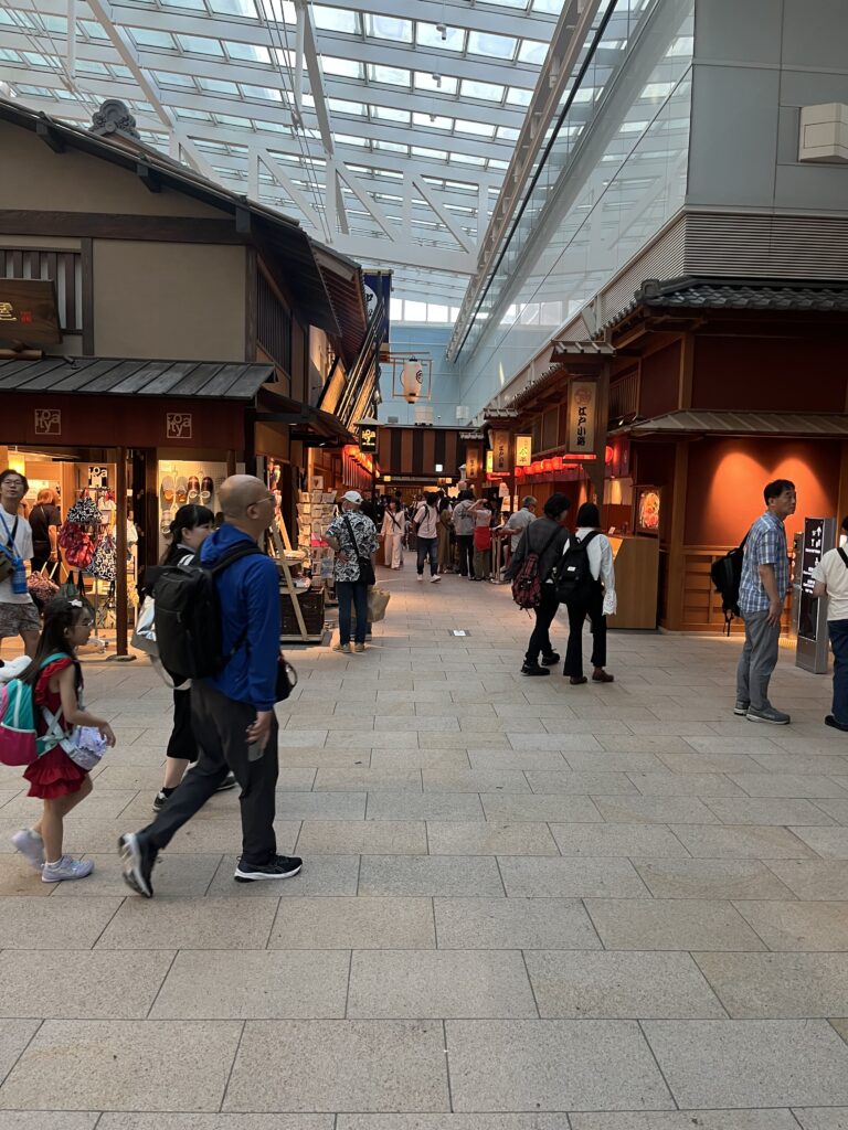 Edo-style shopping street inside Haneda Airport featuring traditional wooden storefronts, lantern lighting, and travelers walking through.