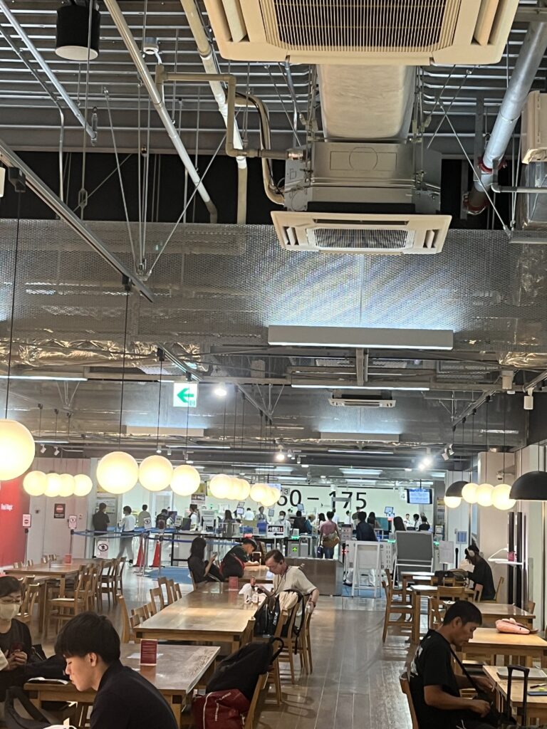 Seating area inside Narita Airport’s low-cost carrier terminal, with wooden tables, pendant lights, and passengers waiting near security checkpoints.