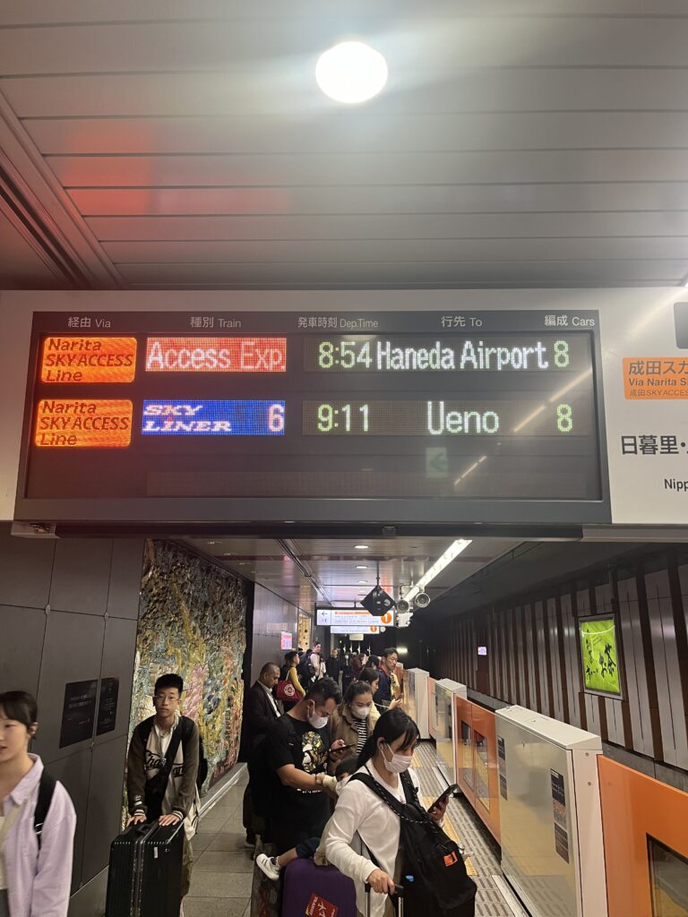 Electronic train departure board on the Narita Sky Access Line showing direct service to Haneda Airport and Ueno.
