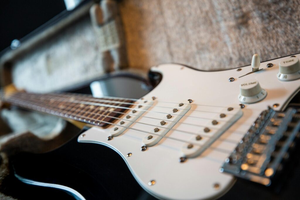 Close-up of a black electric guitar with white pickguard and control knobs resting in a case