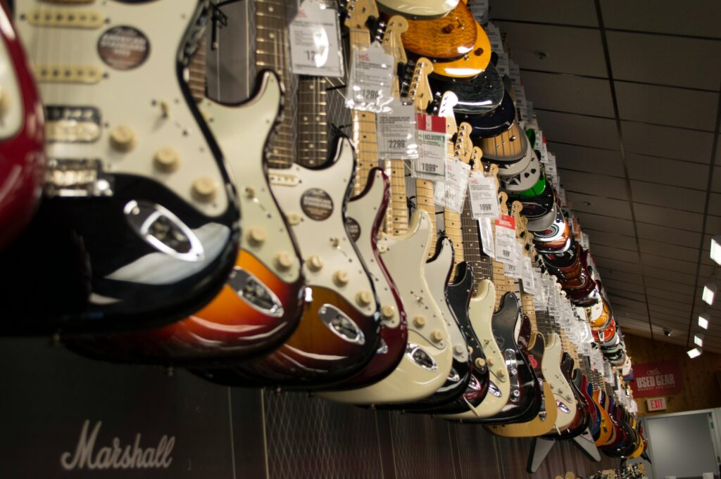 Row of electric guitars hanging in a music store with price tags and amplifiers below