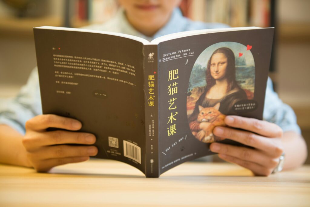 Person reading an art book featuring a Mona Lisa parody with a cat on the cover, highlighting the playful side of contemporary art publications.