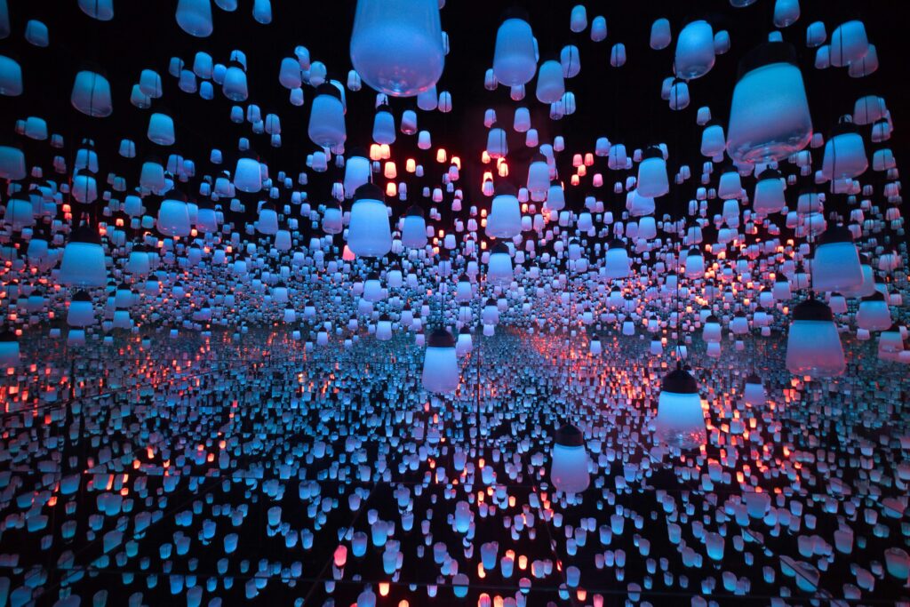 Immersive digital art installation with hundreds of suspended lantern-like lights reflected endlessly across mirrored walls, creating a surreal multimedia museum experience.