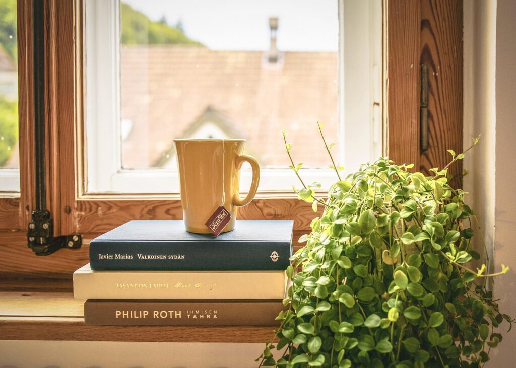 Cozy spring interior by a window with books, a cup of tea, and green plants